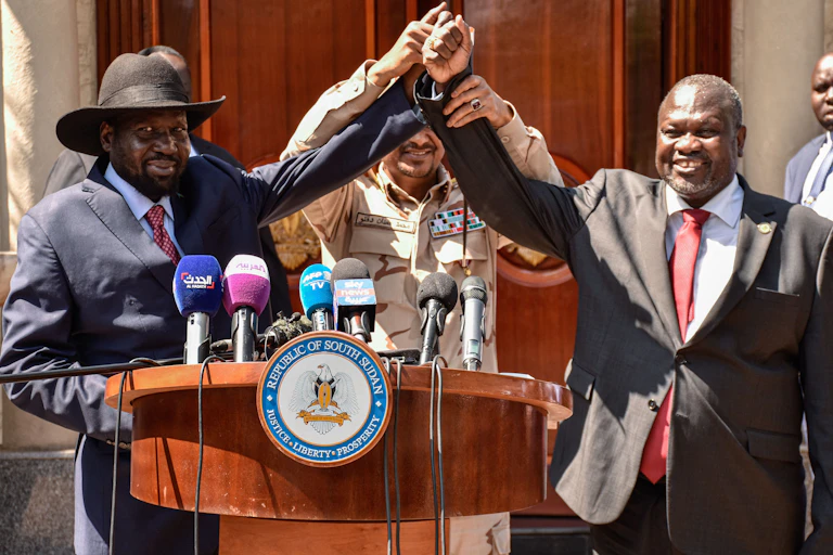 Two men have their hands held together in the middle by a third man as they stand behind a podium with microphones on it