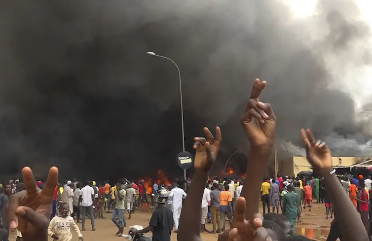 A crowd gathers with smoke in the background.