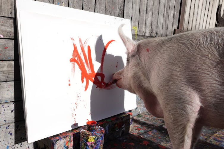A big holding a paintbrush in its mouth paints thick red lines on a canvas.