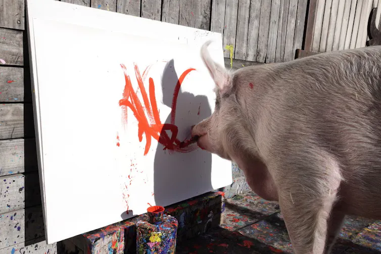 A big holding a paintbrush in its mouth paints thick red lines on a canvas.