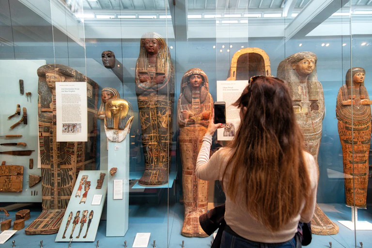 A woman taking a photo of a display case of Egyptian artefacts.