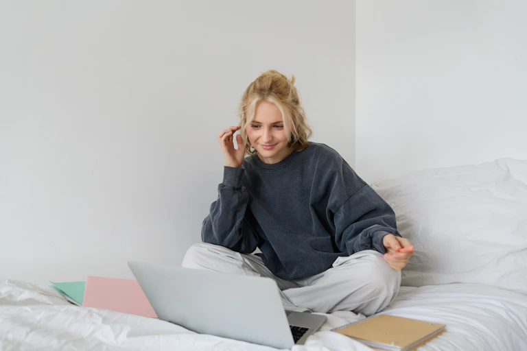 Woman sat on bed looking at laptop