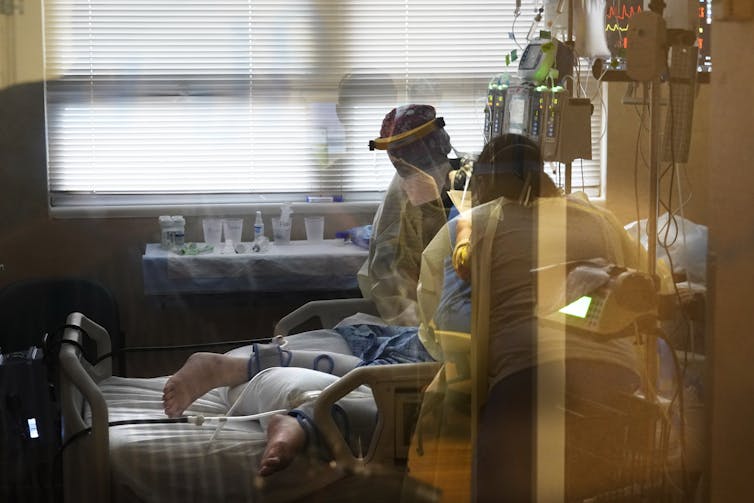 Two health care workers in full PPE attending to a patient lying on hospital bed
