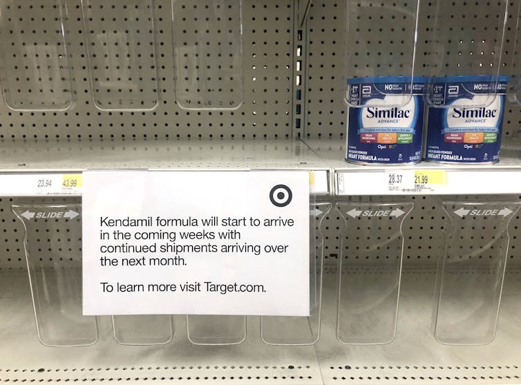 Two containers of baby formula seen on otherwise empty store shelves