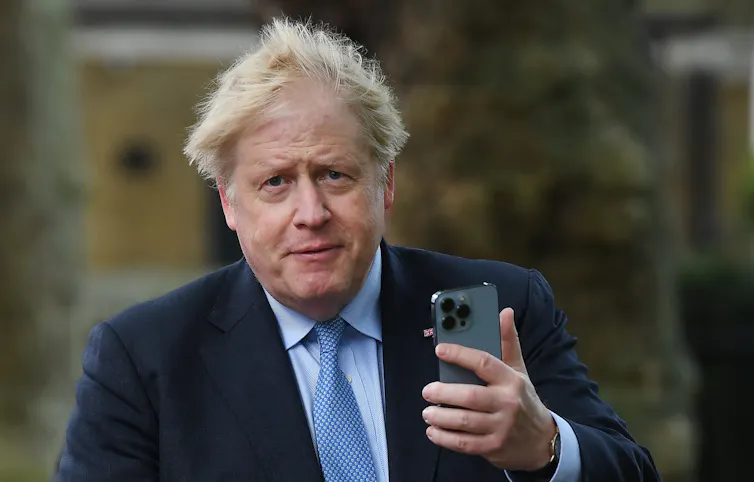 Boris Johnson looking into the camera, holding a mobile phone