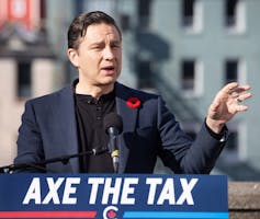 A man in a jacket behind a sign that says axe the tax.