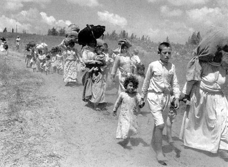 Black and white photo of women and children marching along a dirt road.