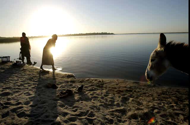 Pessoas lavam roupas na beira do Lago Chade com o pôr do sol sobre a água.