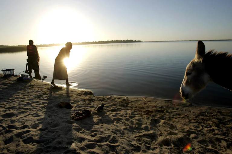 Pessoas lavam roupas na beira do Lago Chade com o pôr do sol sobre a água.