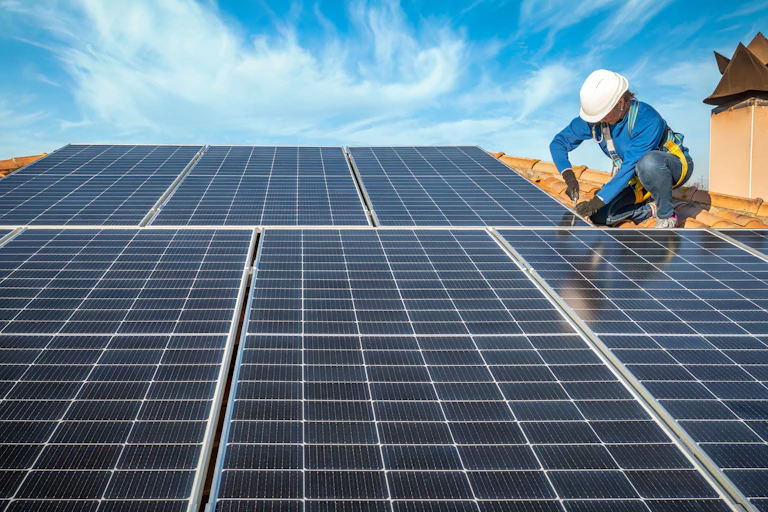 Engineer in blue suit and protective helmet installing photovoltaic panels on a roof system