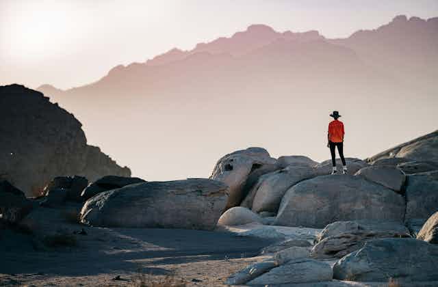 A person standing on a rock formation looking toward a mountain