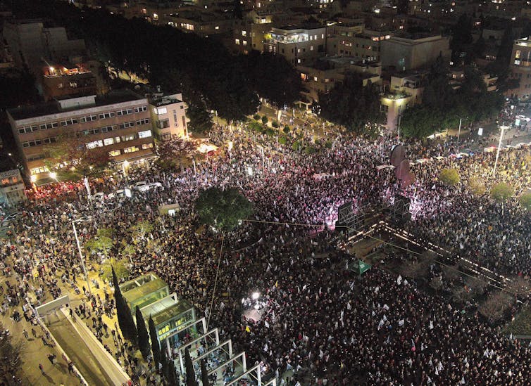 An aerial shot shows thousands of people in a town square