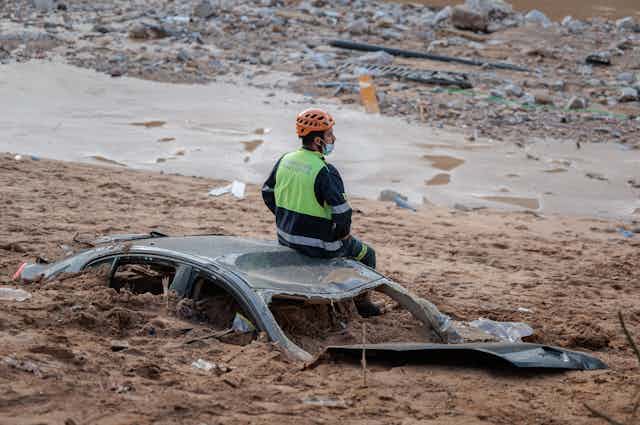 man sitting on car buried in mud.