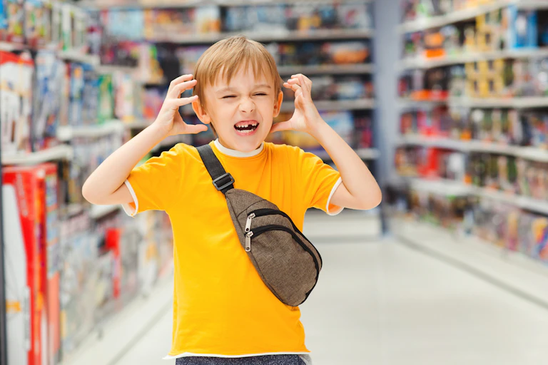 Overwhelmed boy in supermarket about to put hands on ears