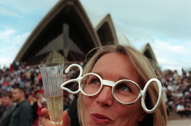 A woman holding a glass of champagne wearing novelty glasses that say 2000