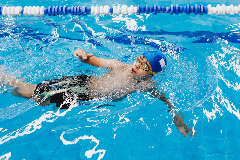 A boy swims freestyle in a pool with a lane rope.