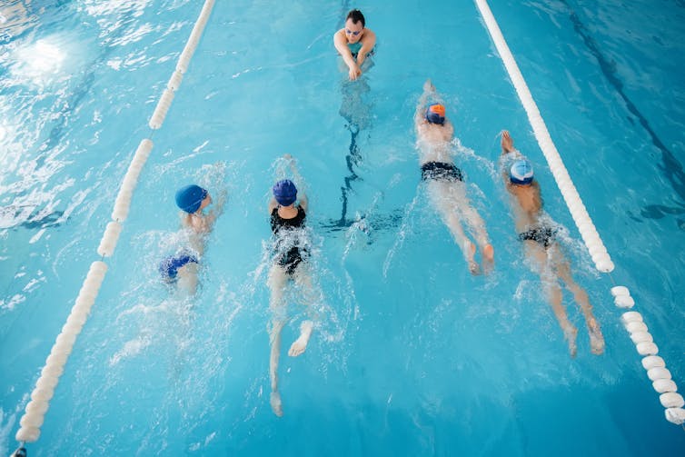 A group of four older children have a lesson in a pool with a teacher.