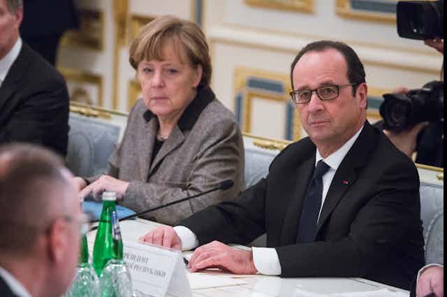 Angela Merkel and François Hollande sat next to each other at a table.