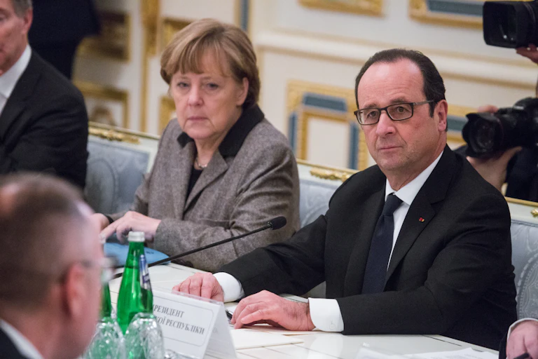 Angela Merkel and François Hollande sat next to each other at a table.