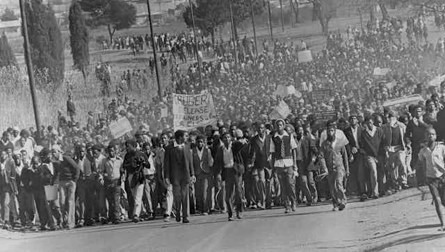 A sea of young Africans, some win school uniforms, marches down a road, placards, banners and fists aloft.