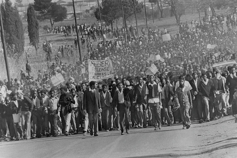 A sea of young Africans, some win school uniforms, marches down a road, placards, banners and fists aloft.