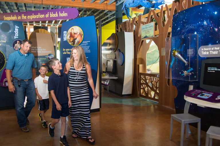 A mom, dad and two sons walk through an exhibit at a museum.
