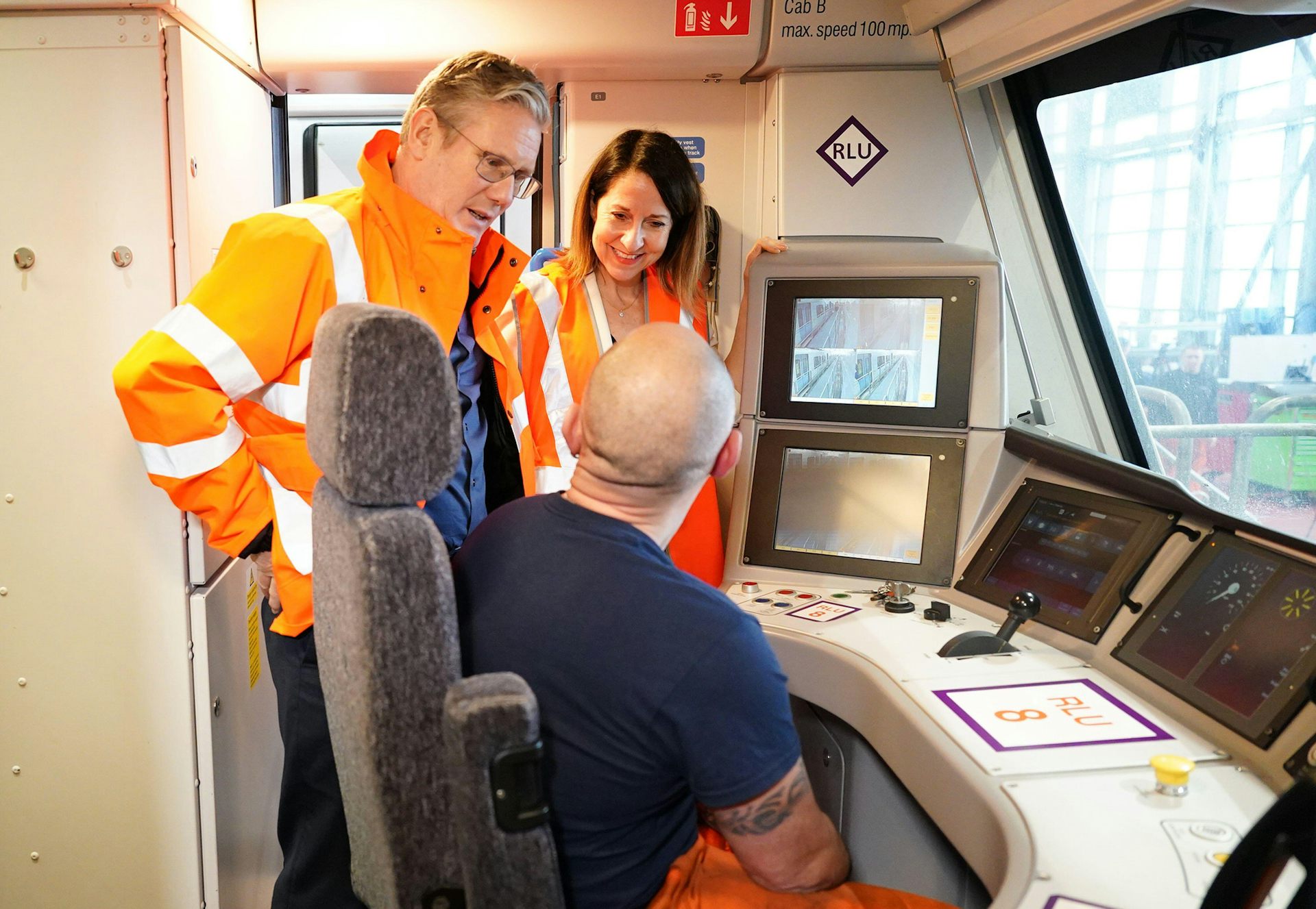 Starmer and Kendall in hi vis jackets, speaking to a train operator inside a carriage