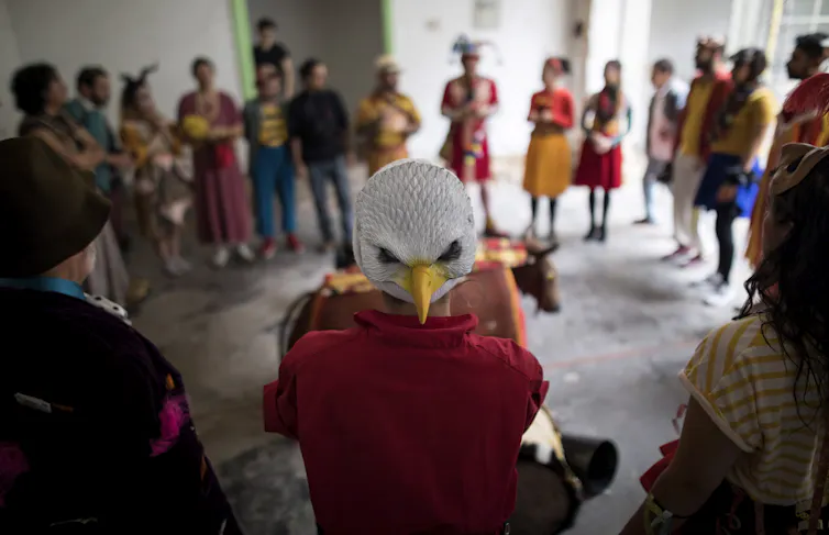 An eagle mask seen on a face of costumed people with others in a circle.