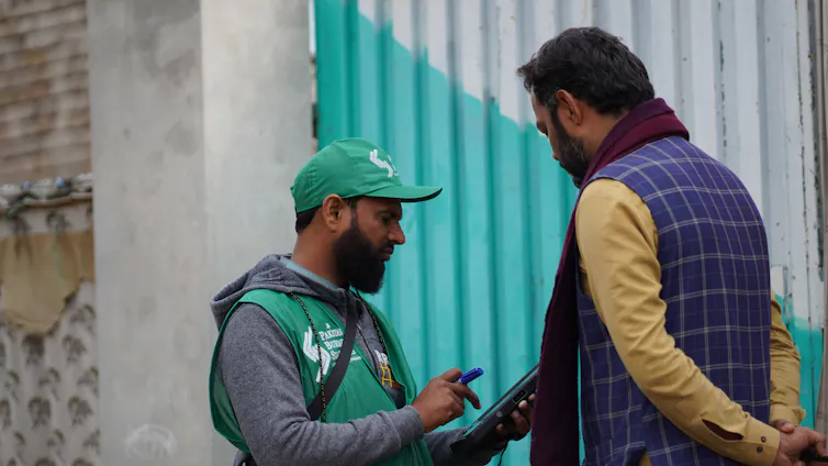 two pakistan men standing in street, one with census clipboard