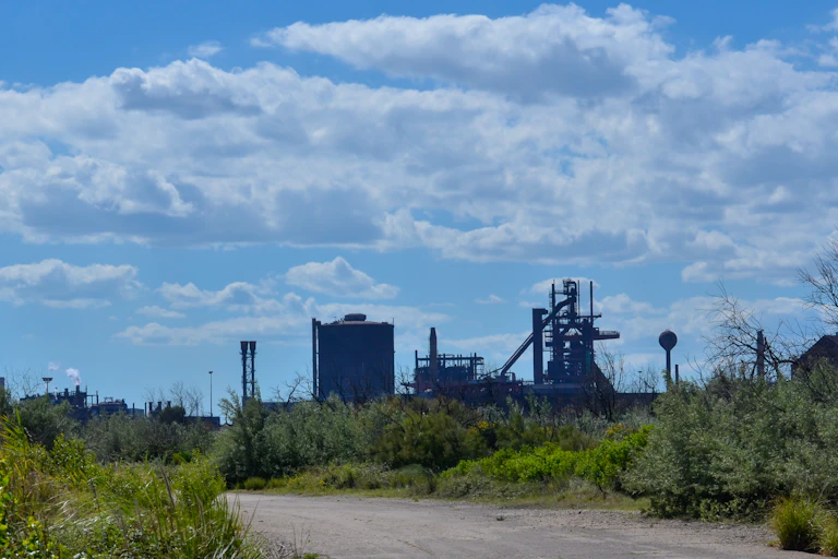 un site industriel au fond avec au premier plan, une route et une végétation mal entretenue