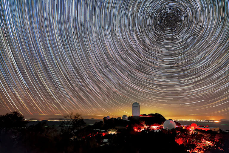 Timelapse photo showing star trails in the night sky above a large telescope building.