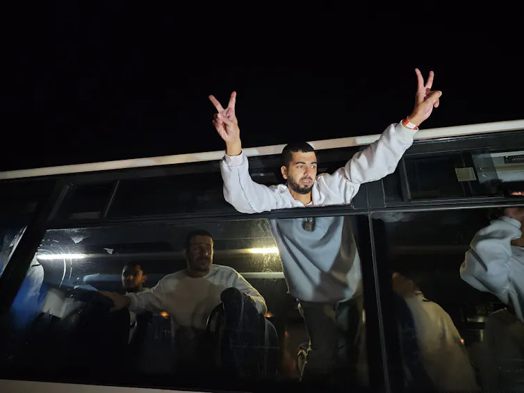 A man flashes 'V' peace signs from inside a bus.
