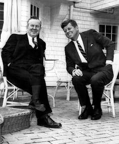 Two men in suits and ties sitting on patio furniture.