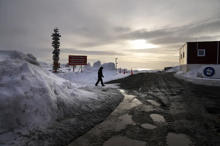 A lone figure walking across ice near a research base.
