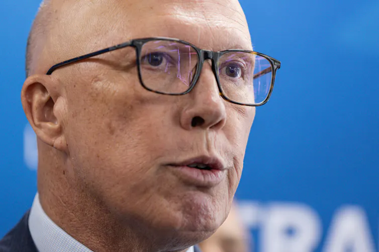 Peter Dutton's head, wearing glasses, in front of a blue banner