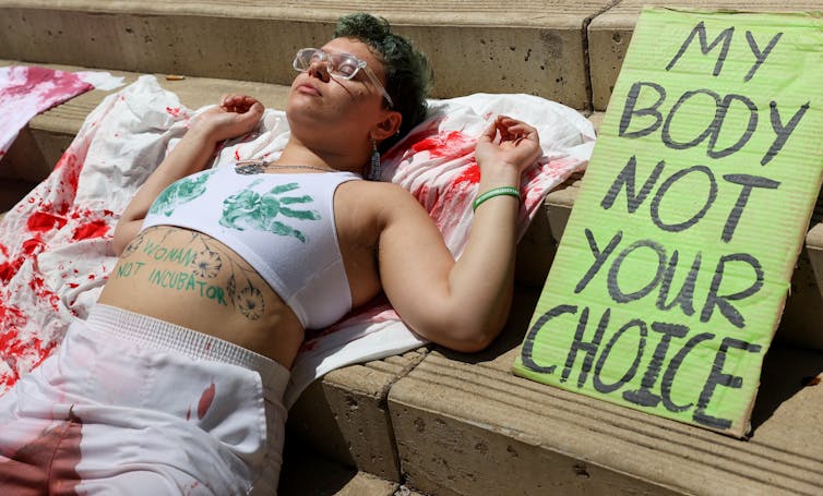 An abortion rights protestor lays on a sheet with the words woman not incubator written on her stomach at the federal courthouse in Austin Texas.