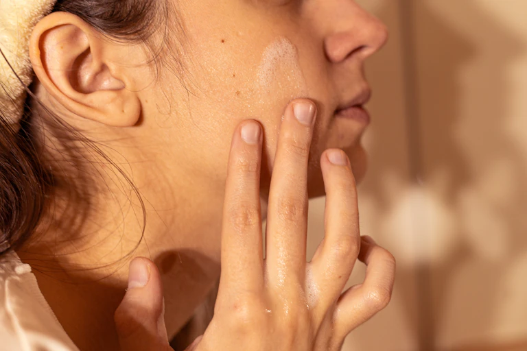 Teen girl rubs foaming cleanser into her face.