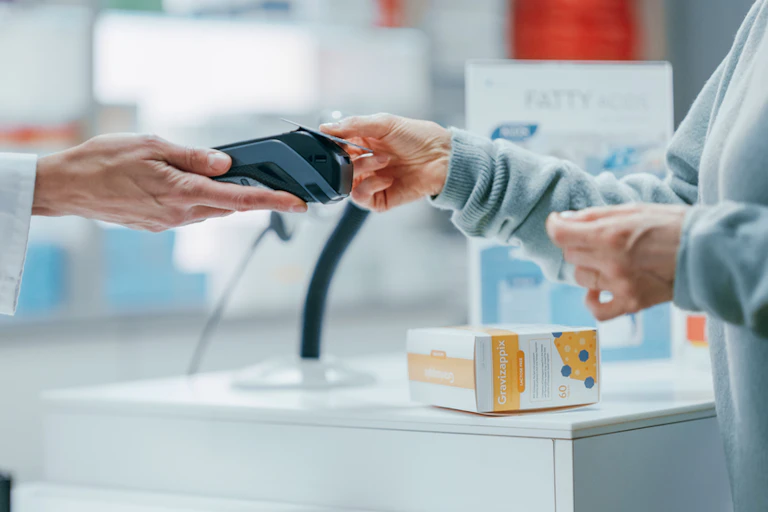 Person paying for medicine with card at pharmacy counter, pharmacist holding out card reader