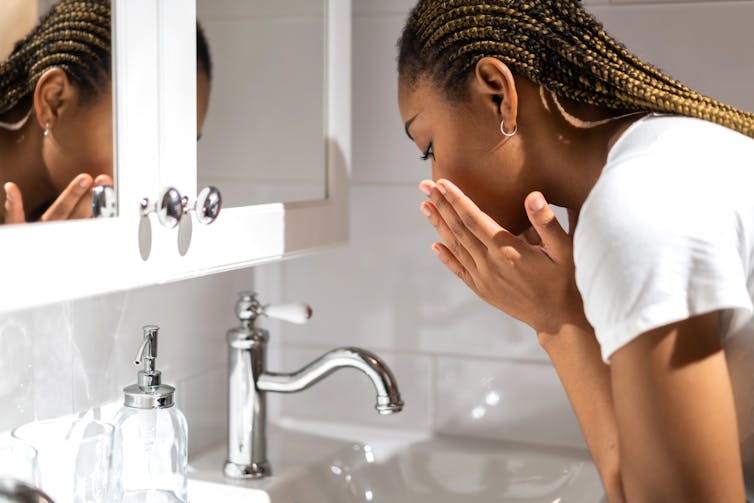Teen girl washes her face at the bathroom sink.