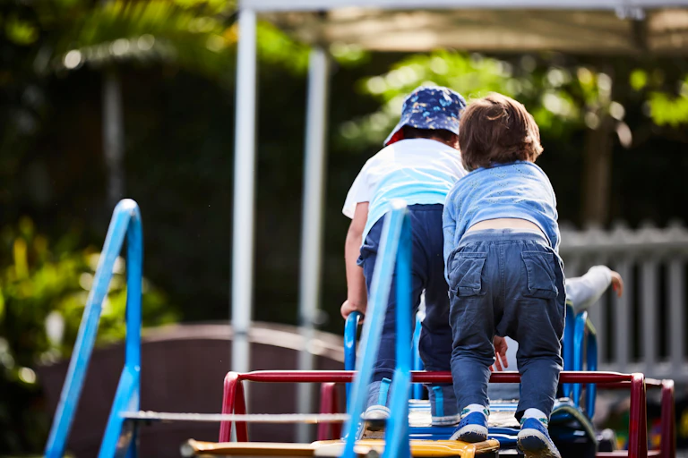 Two young children climb on a play equipment.