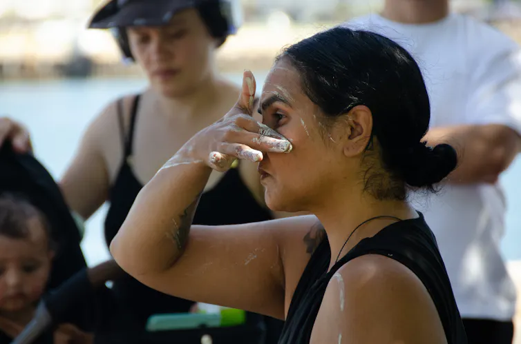 A woman puts white pigment on her cheaks.