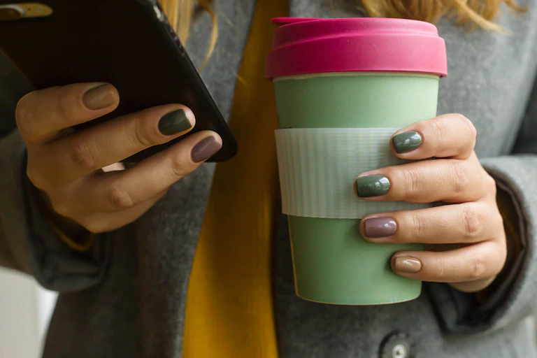 A woman holding a keep cup and a mobile phone