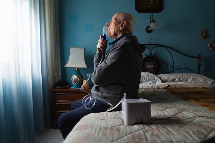 A man sitting on a bed using a breathing machine.