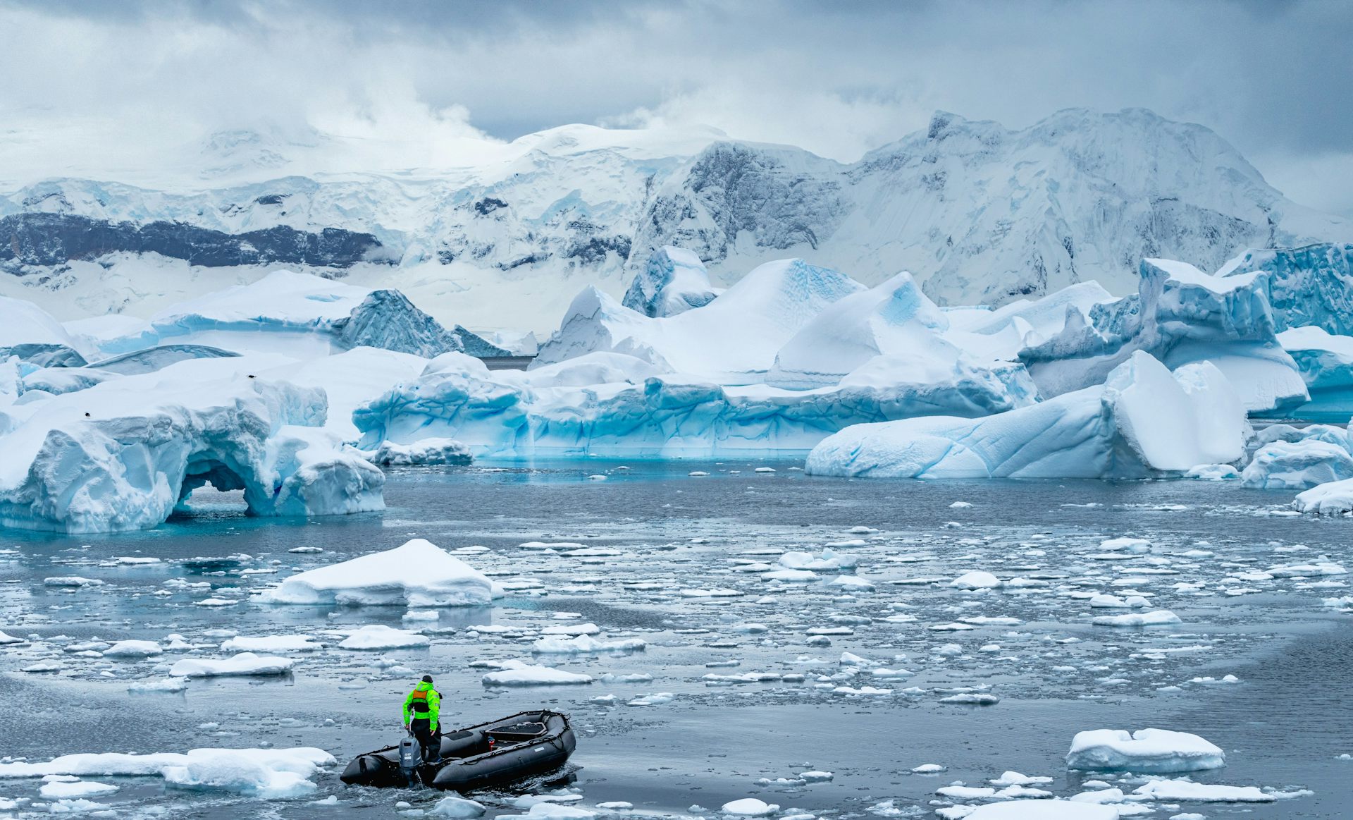 A small boat drives through melted ice with a backdrop of ice bergs and shelves.