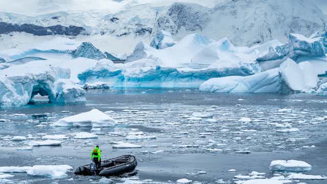 A small boat drives through melted ice with a backdrop of ice bergs and shelves.