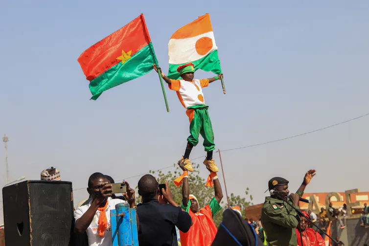 A boy raised above a crowd as he waves the flags of Burkina Faso and Niger.