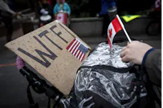 La señal que lee VTF con la bandera estadounidense y una persona que sostiene la bandera mini canadiense en la protesta.