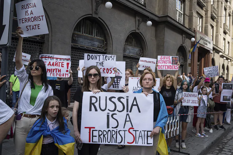 Protesters line a city street. One sign reads Russia is a Terrorist State.