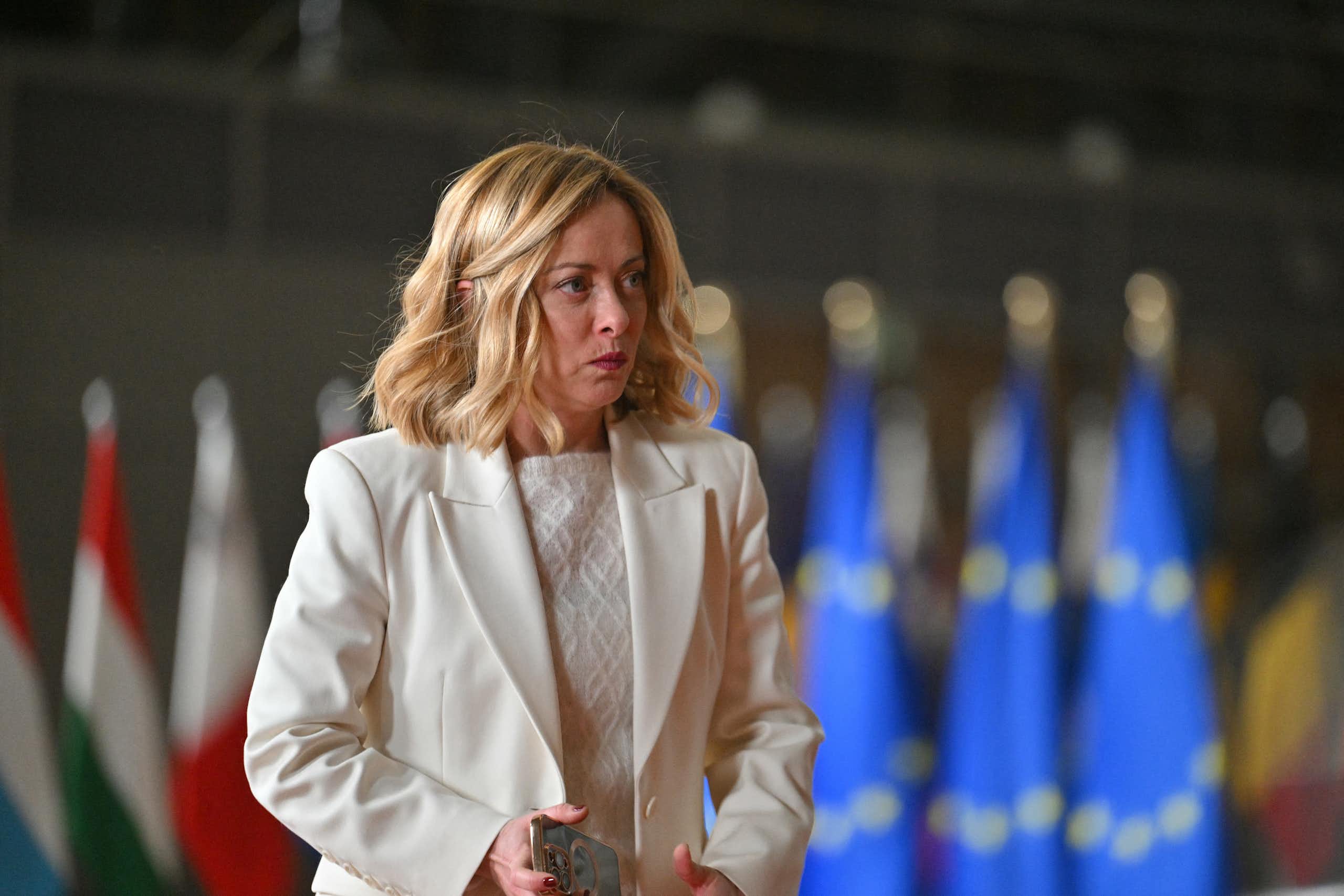Italy's Prime Minister Giorgia Meloni is seen in front of a row of flags, including three blue European Union ones.