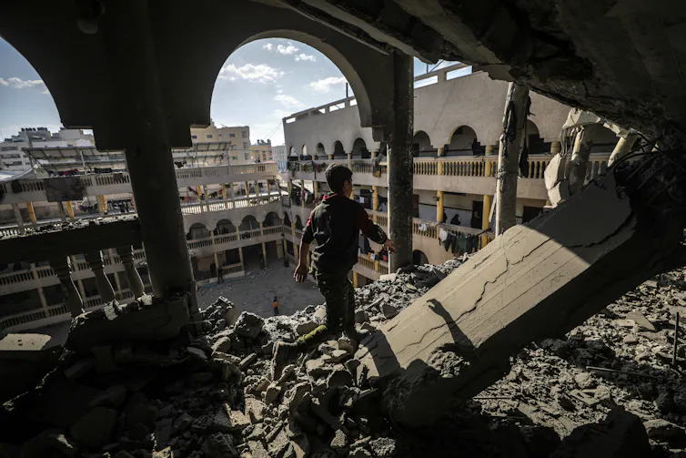 A boy looks out of an upper floor of a badly damaged building in Khan Younis at the rubble of other buildings.